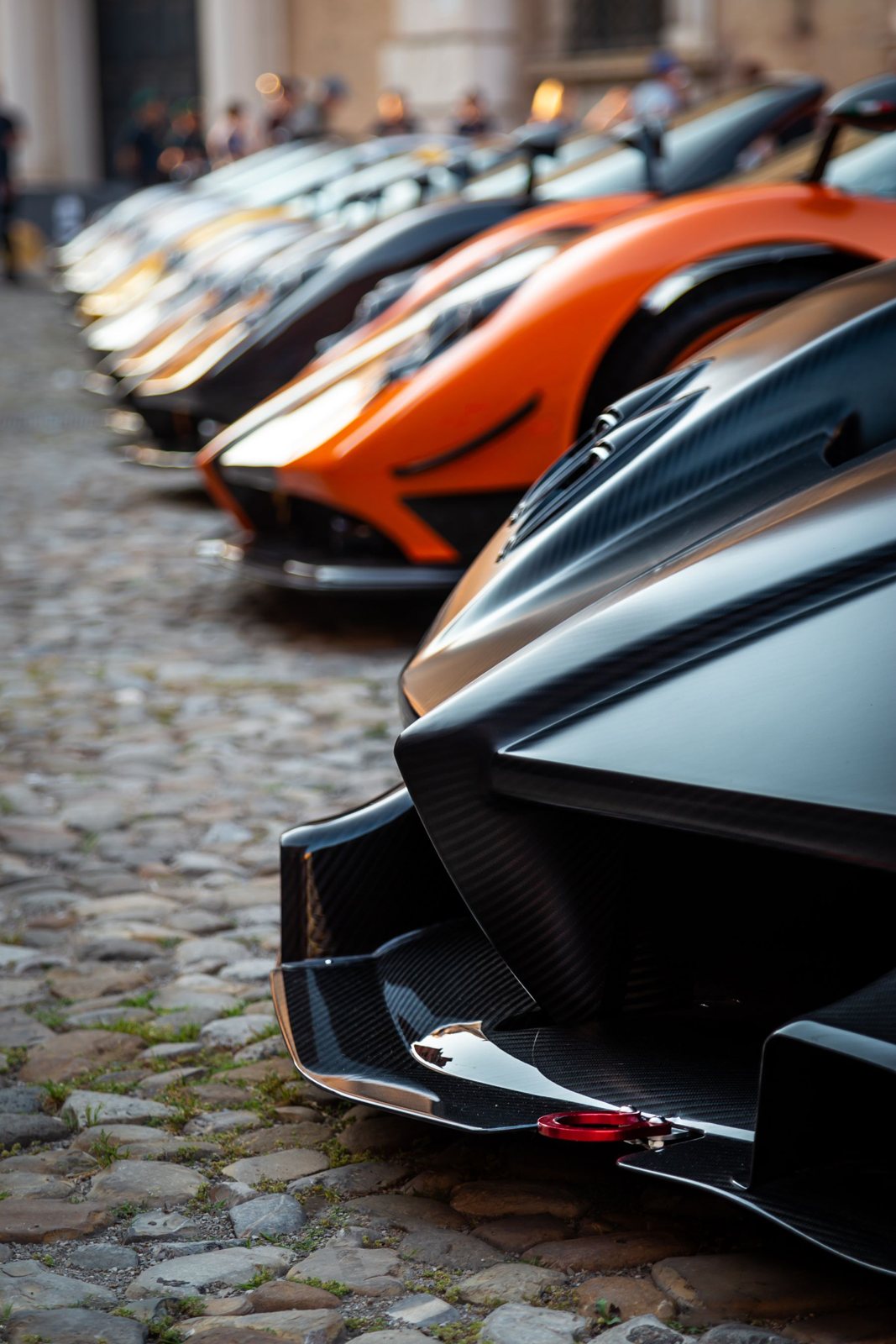 A long row of luxury supercars on a cobblestone street